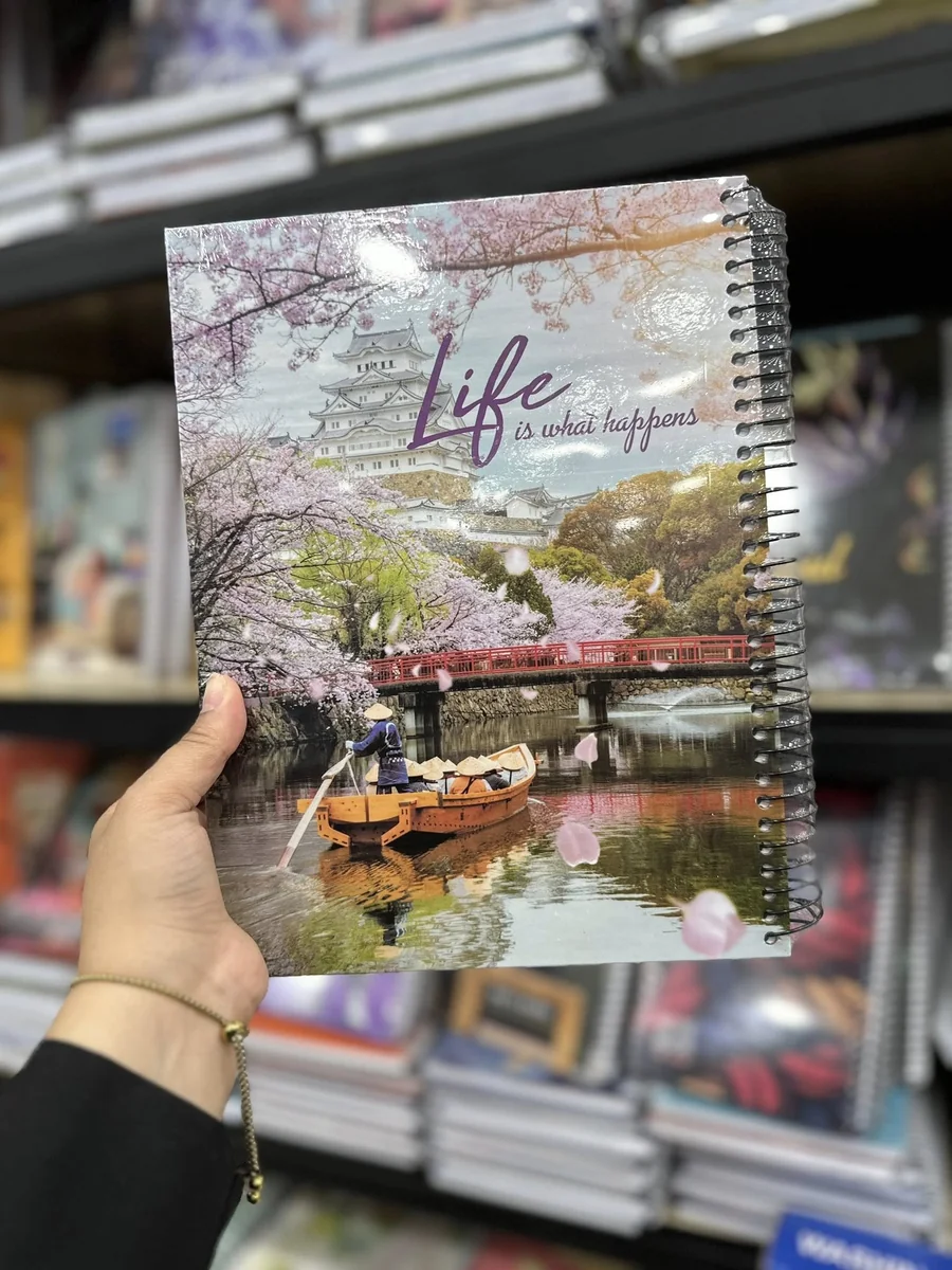 دفتر ملاحظات سلكي يتميز بغلاف مطبوع عليه لوحة فنية لجسر وقارب وسط أزهار الكرز الوردية والبيضاء.